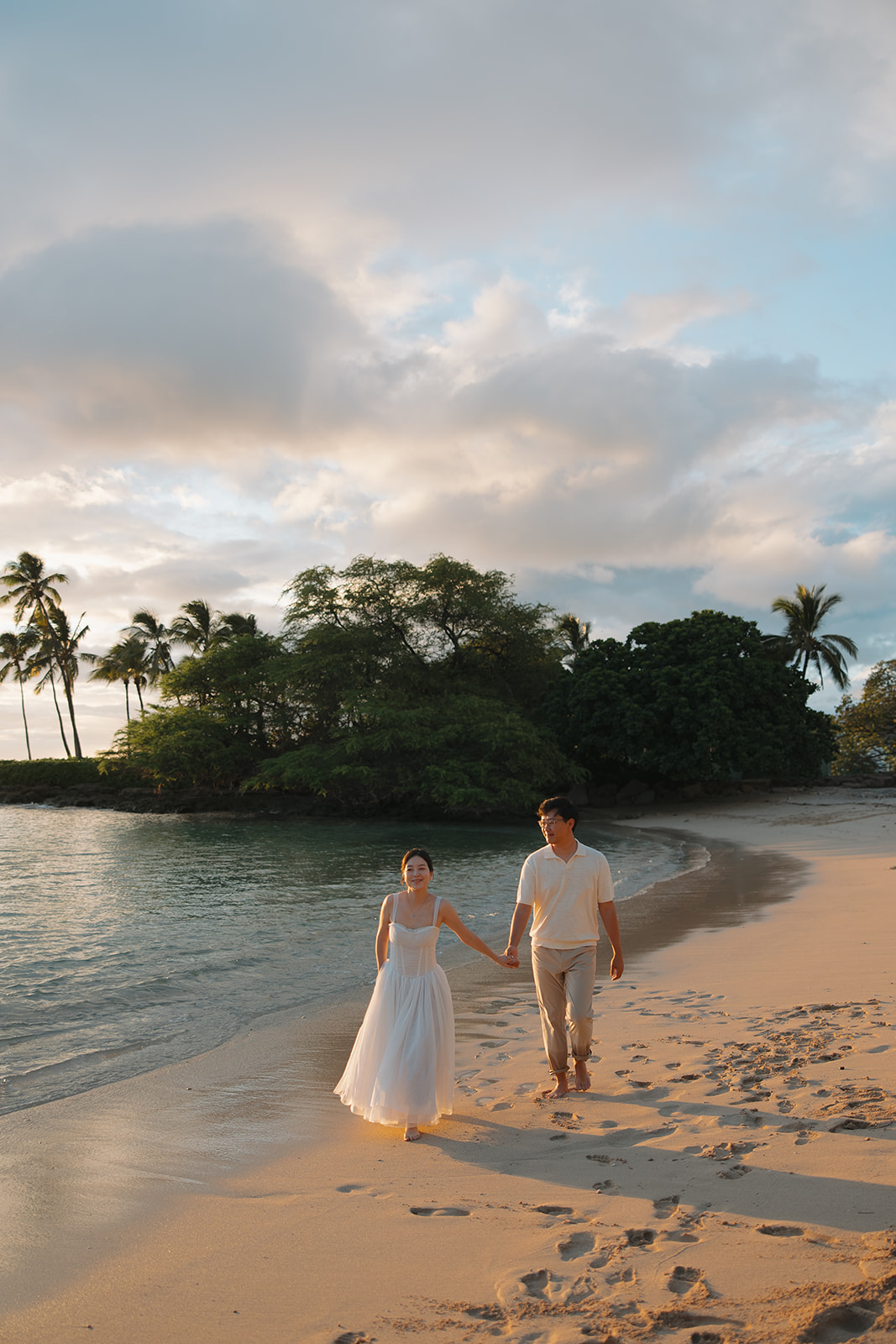 Lisa and Sergei walking hand in hand along a quiet Hawaii shoreline at golden hour